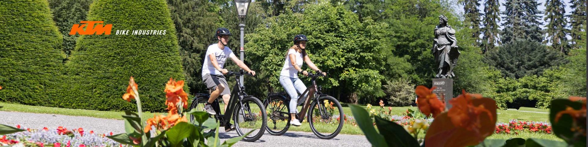 Zwei Personen fahren mit KTM E-Bikes durch einen Park